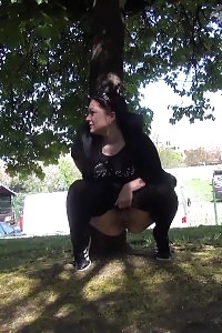 Black haired lady is filmed peeing by a tree