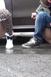 2 gfs piss behind a parked vehicle